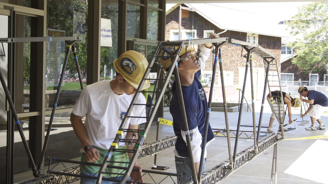 Two volunteers working on a long metal frame outside a building