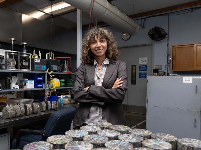 Somayeh Nassiri with arms crossed standing behind trays of pavement samples in a lab.