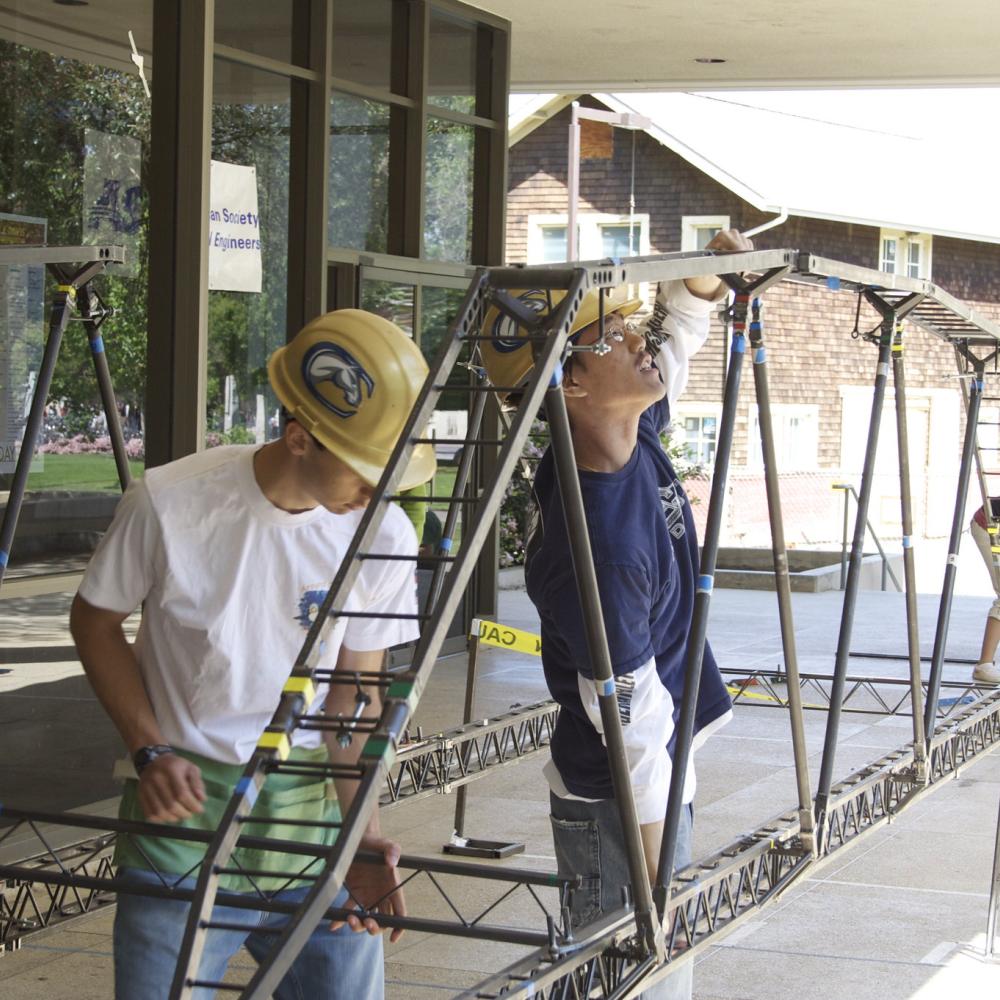 Two volunteers working on a long metal frame outside a building