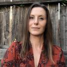 Woman with brown hair wearing red shirt with wooden fence in background