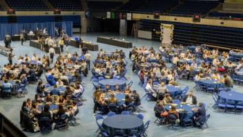 Wide shot of a banquet hall with many different circular tables and students clustered around them