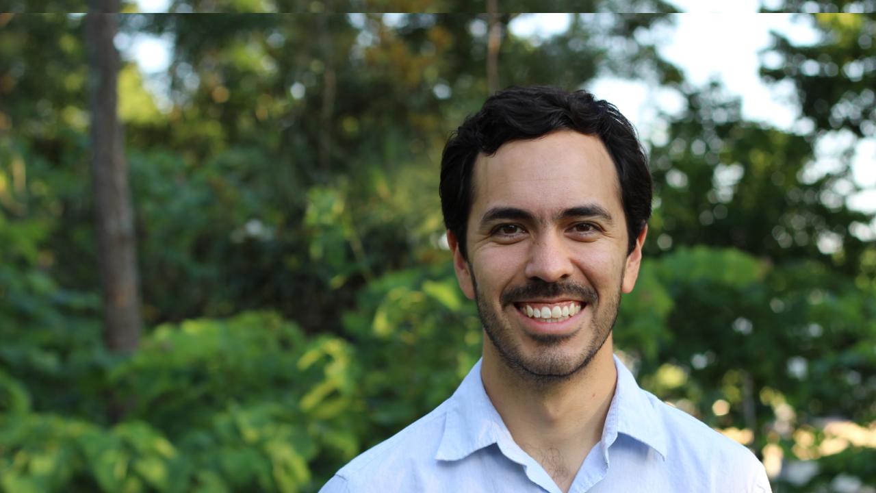 Image of a man smiling in front of greenery and trees