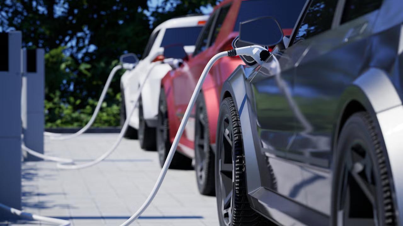 Electric cars charging at a station, with cables connected and greenery in the background.