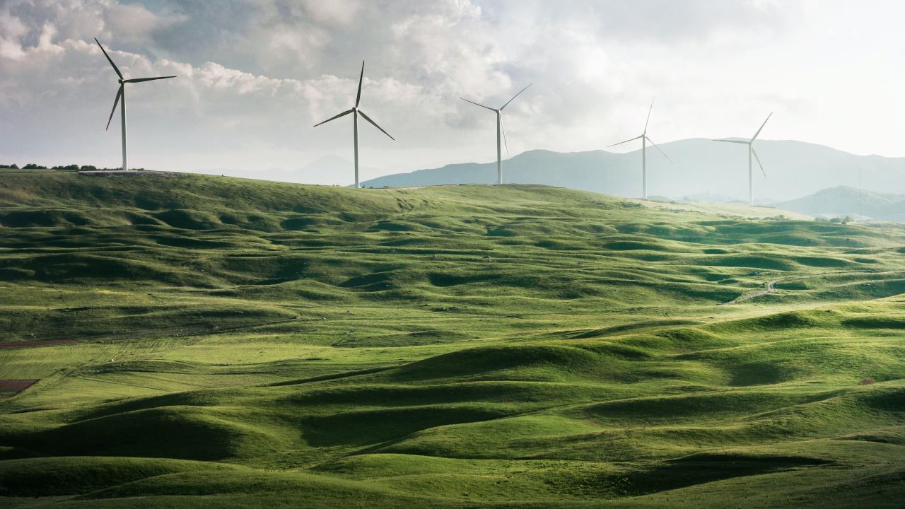 Green hills against a partly cloudy sky, with windmills in the background.