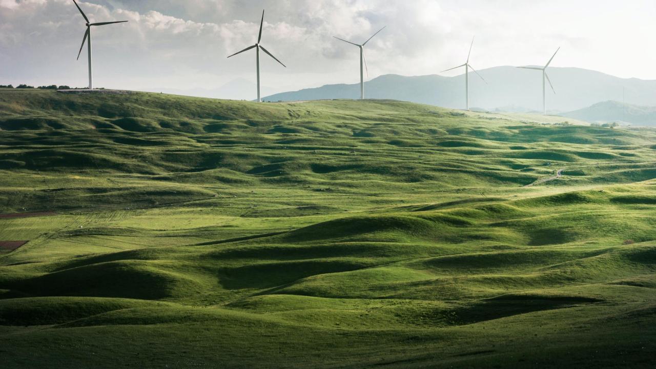 Green hills against a partly cloudy sky, with windmills in the background.
