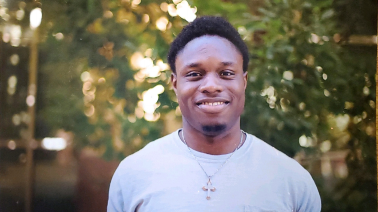 Image of dark skinned man with black hair against a blurred background of trees