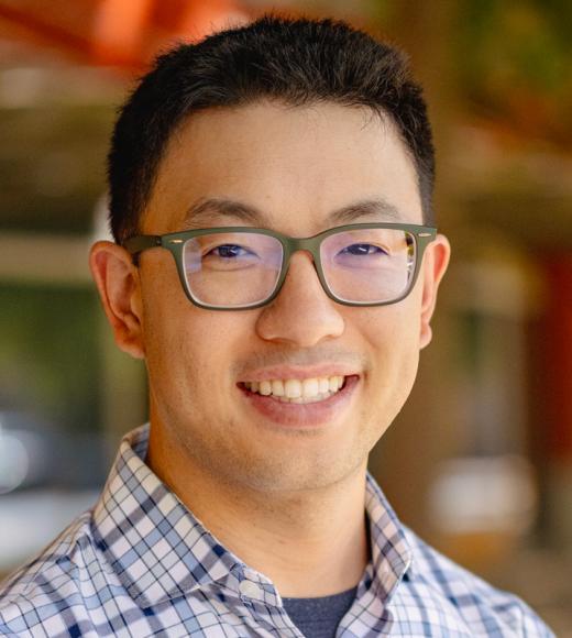 A man with black hair and glasses smiles at the camera