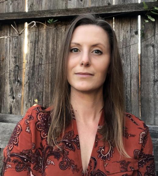 Woman with brown hair wearing red shirt with wooden fence in background