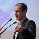 Kaveh Madani in suit speaking at podium with microphones and floral arrangement