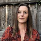 Woman with brown hair wearing red shirt with wooden fence in background
