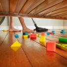 Photograph of someone vacuuming a wooden floor under a couch, with children's blocks on the floor
